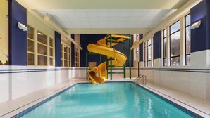 Una piscina con un tobogán en espiral amarillo, ventanas amplias y suelo de baldosas.
