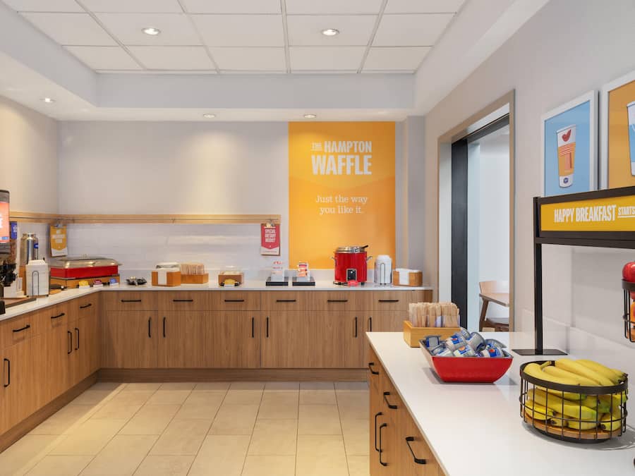 A modern kitchen area with a central counter, various appliances, and a sign indicating a waffle station.