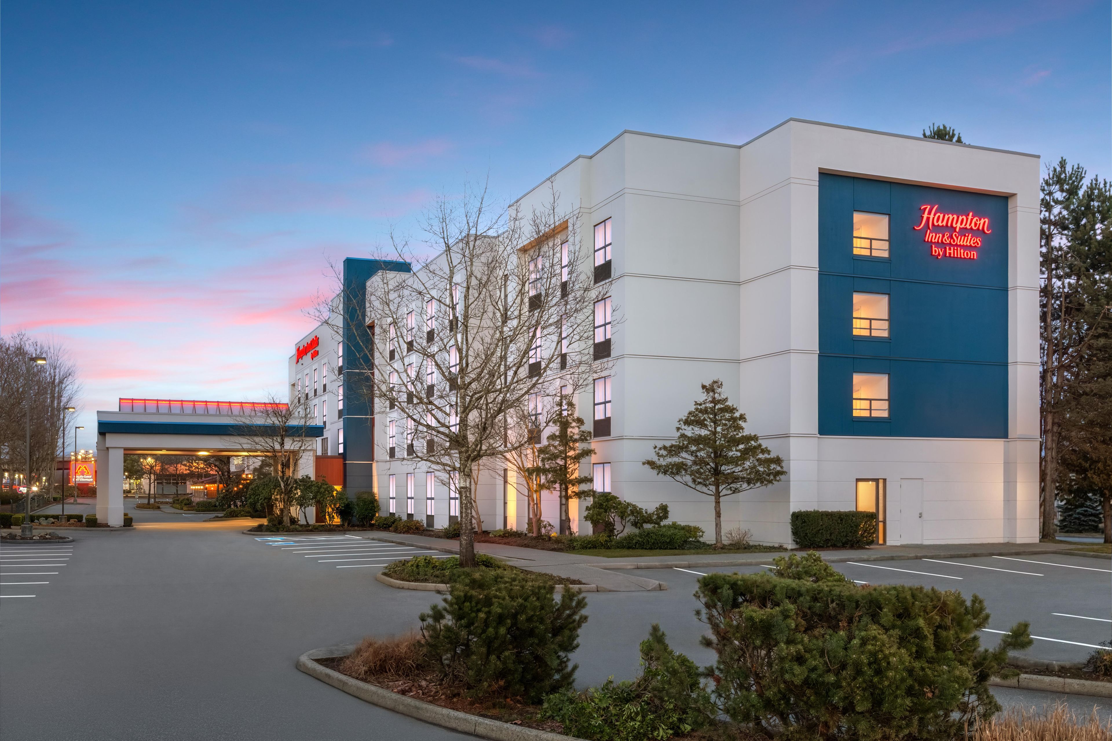 A modern hotel with a prominent Hampton Inn & Suites sign, a parking lot, and a landscaped entrance area.