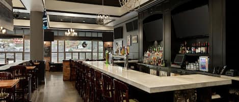 A bar area with a long counter, multiple seating options, and a variety of bottles and glasses.