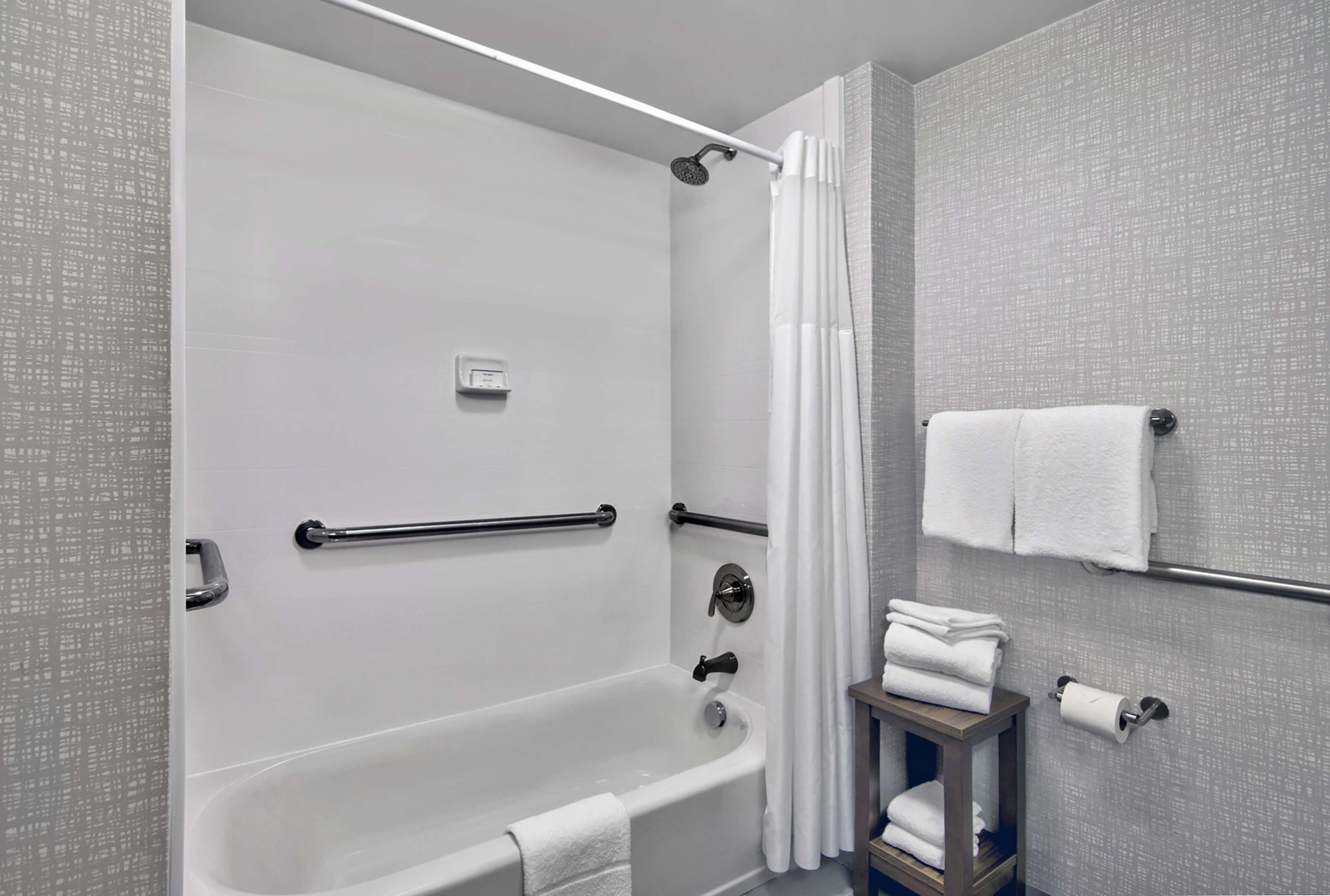 A modern bathroom with a walk-in shower, grab bars, a towel rack, and a toilet paper holder.