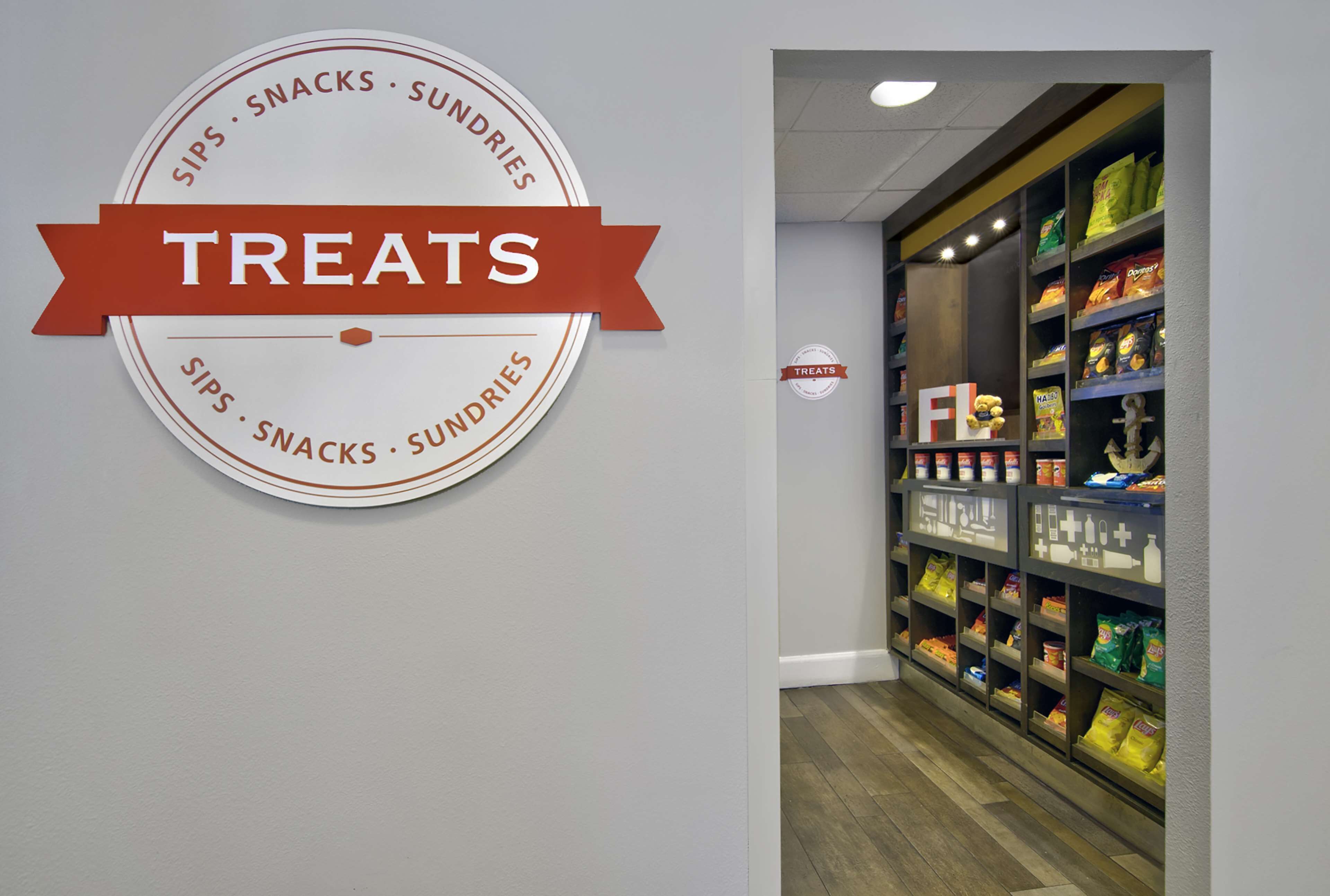 Un letrero en la pared con la palabra 'TREATS' y un logotipo circular que dice 'SIPS • SNACKS • SUNDRIES'.