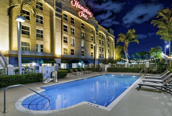 A pool area with lounge chairs, a pool with a 3 ft 3 in. depth marker, and a Hampton Inn building with a neon sign. - Hampton Inn Ft. Lauderdale Airport North Cruise Port (Fort Lauderdale)