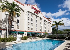 A Hampton Inn hotel with a swimming pool, palm trees, and a clear blue sky. - Hampton Inn Ft. Lauderdale Airport North Cruise Port (Fort Lauderdale)