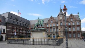A cobblestone square with a statue of a figure on horseback, surrounded by historic buildings with multiple windows and a clock tower. - AltDüsseldorf (Düsseldorf)