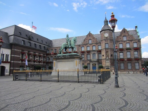 Una plaza adoquinada con una estatua de un jinete, rodeada de edificios históricos con numerosas ventanas y una torre del reloj.