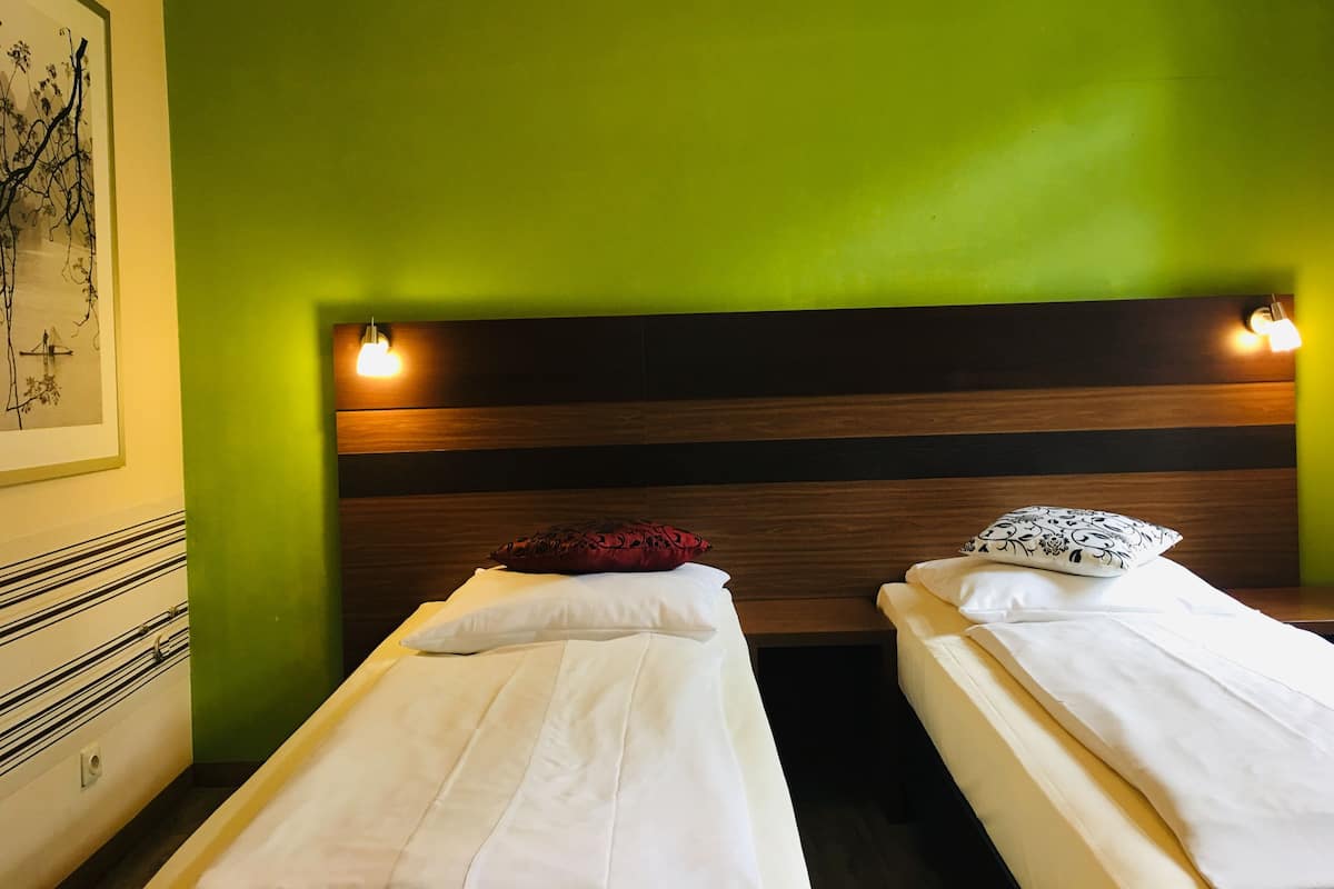 A room with two single beds, each with a pillow and a bedside lamp.