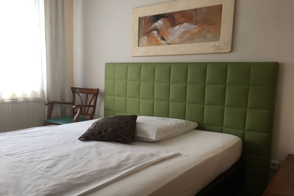 A neatly made bed with a green headboard, a single decorative pillow, and a framed artwork above it.