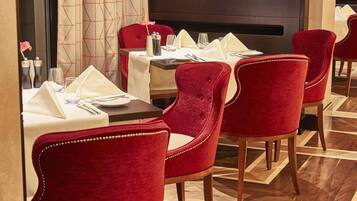 A restaurant with red velvet chairs, white tablecloths, and a geometric patterned wall.