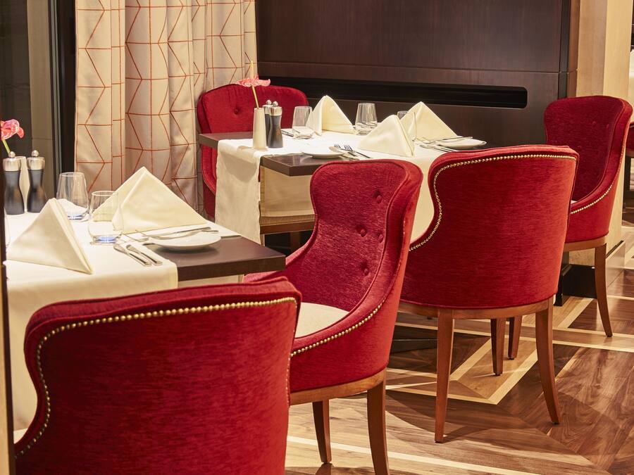 A restaurant with red velvet chairs, white tablecloths, and a geometric patterned wall.