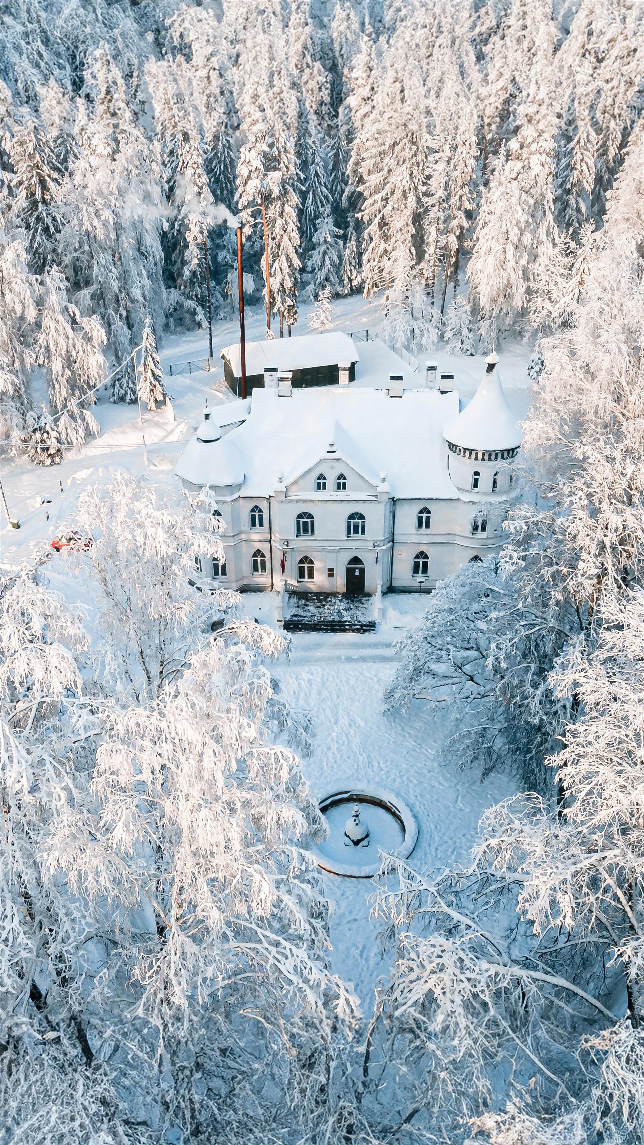 A large, snow-covered building with a symmetrical facade, a central entrance, and a circular fountain in the foreground.