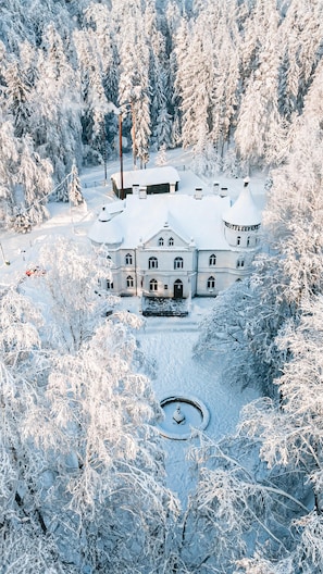 A large, snow-covered building with a symmetrical facade, a central entrance, and a circular fountain in the foreground.