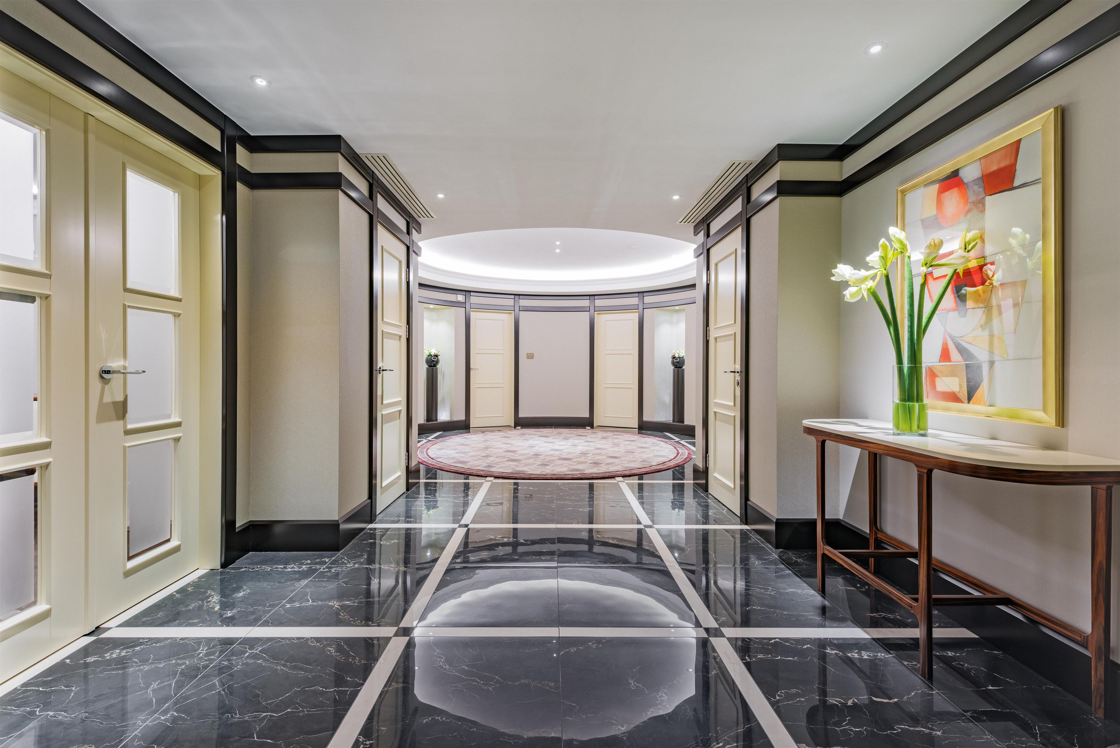 A hotel lobby with a marble floor, a central round carpet, and a painting on the wall.