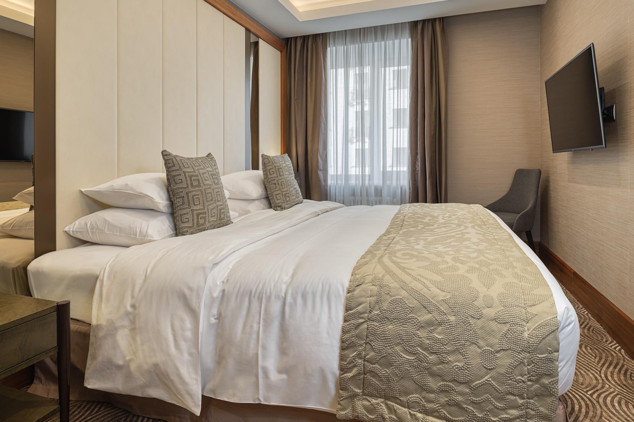 Habitación de hotel con una cama grande, un televisor de pantalla plana montado en la pared y vistas al exterior por la ventana.