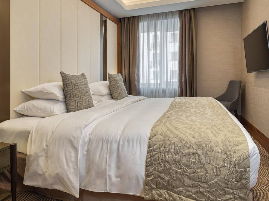Habitación de hotel con una cama grande, un televisor de pantalla plana montado en la pared y vistas al exterior por la ventana.