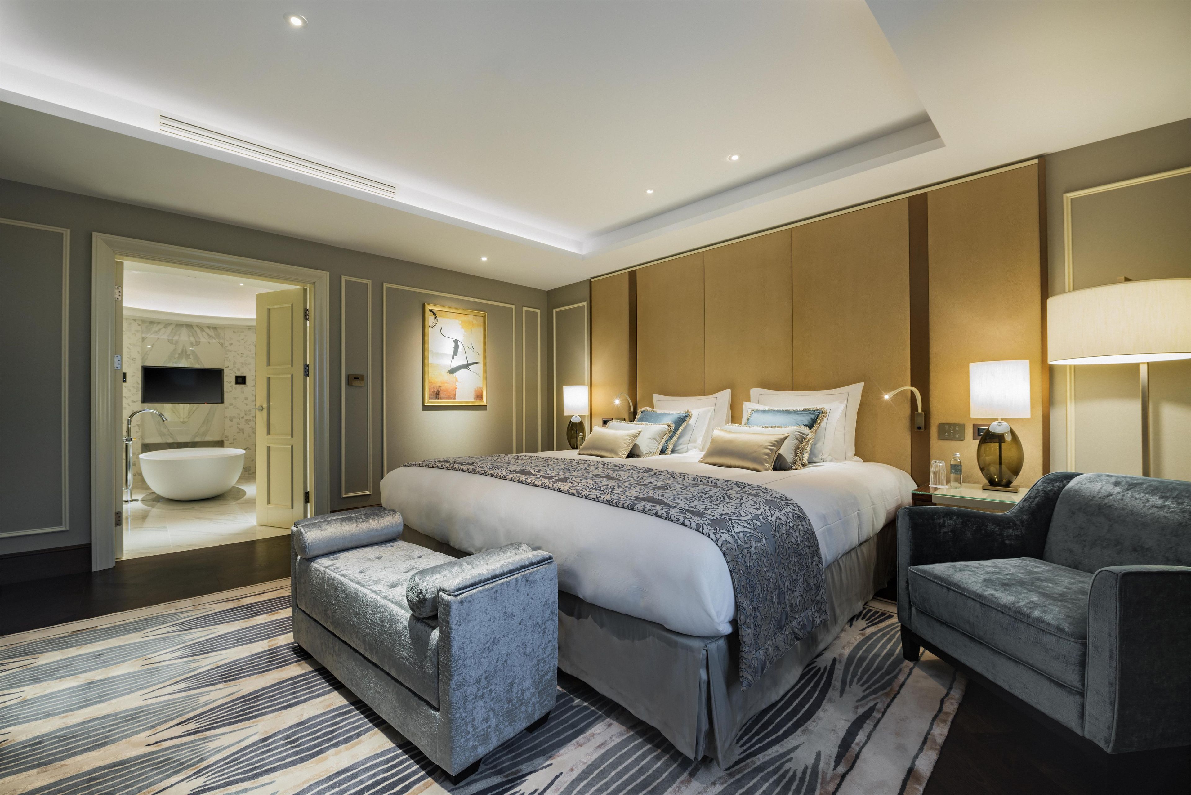 A hotel room with a large bed, a sitting area with a chair, a desk, and a bathroom with a bathtub.