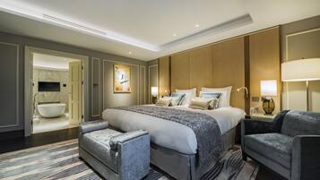 A hotel room with a large bed, a sitting area with a chair, a desk, and a bathroom with a bathtub.