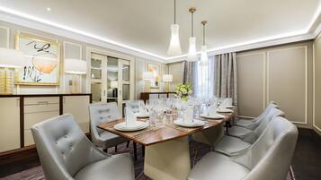 A hotel dining room with a round table set for six, grey upholstered chairs, and pendant lighting.