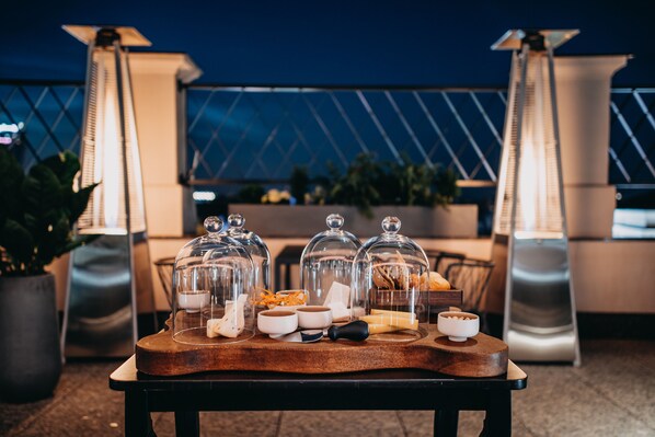 A buffet setup with food items under glass domes, a wooden serving board, and a modern outdoor seating area with metal chairs and potted plants. - Grand Hotel Kempinski Riga (Riga)