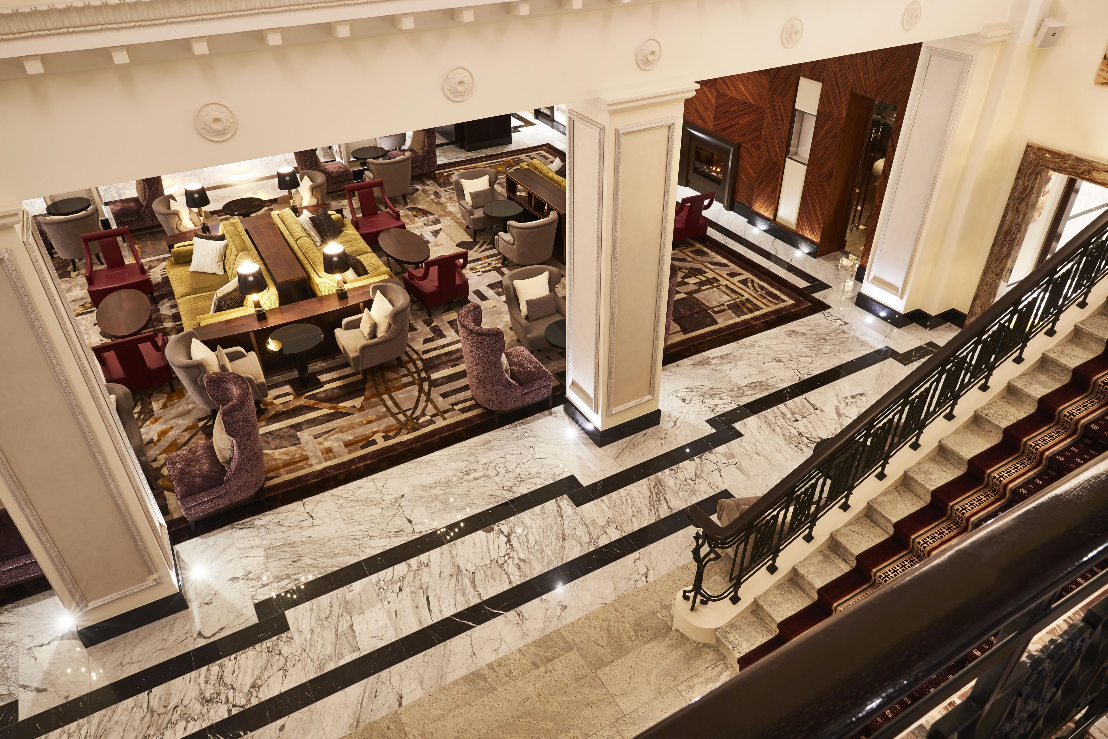 En hotellobby med en trappa i marmor, flera sittgrupper och en storslagen trappa som leder upp till en övre våning.