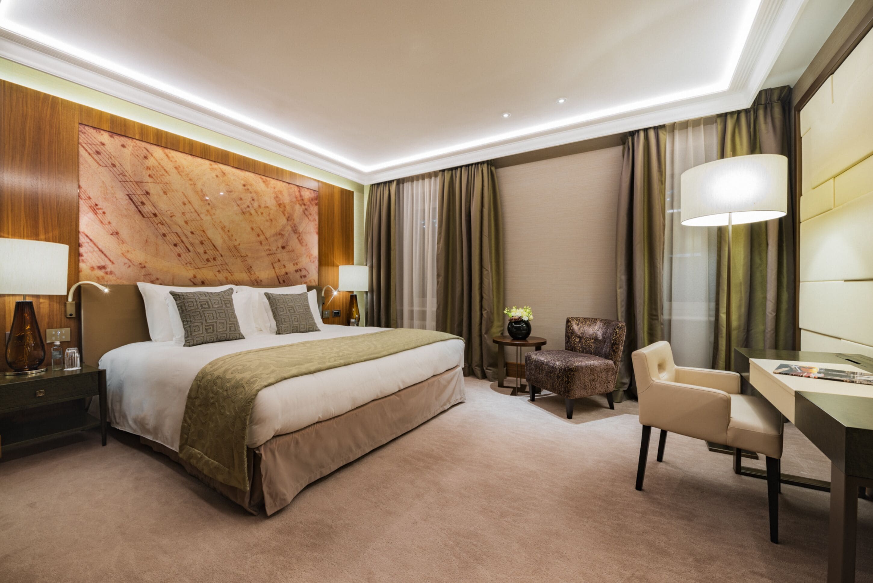 Habitación de hotel con una cama grande, dos mesitas de noche con lámparas, un escritorio con una silla y un panel decorativo en la pared.