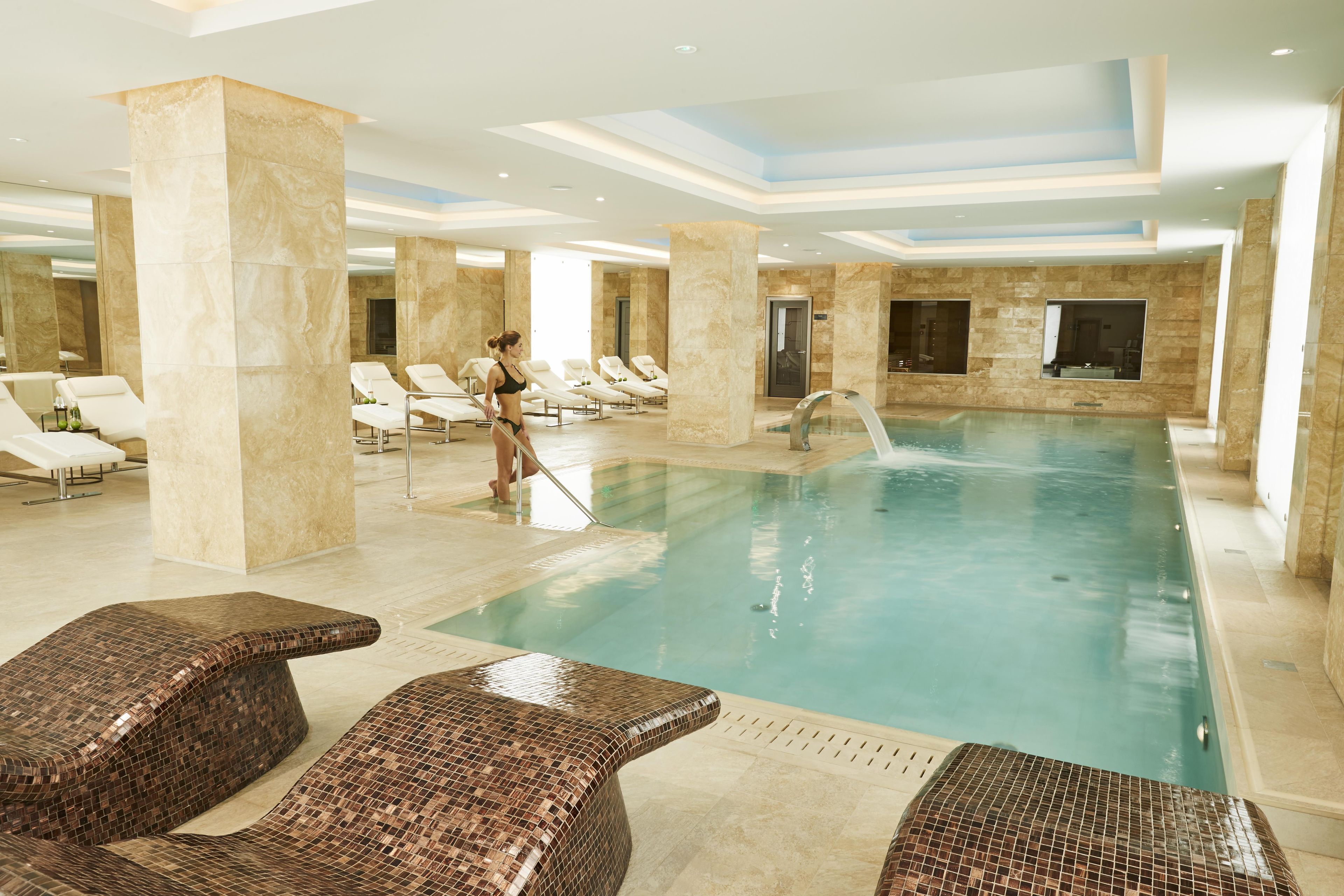 A large indoor swimming pool with multiple lounge chairs and a person cleaning the pool.