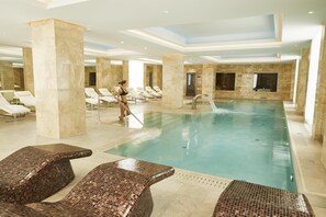 A large indoor swimming pool with multiple lounge chairs and a person cleaning the pool. - Grand Hotel Kempinski Riga (Riga)