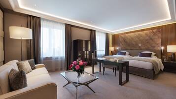 A modern hotel room with a bed, a sofa, a glass coffee table with flowers, a desk, and a large marble wall.