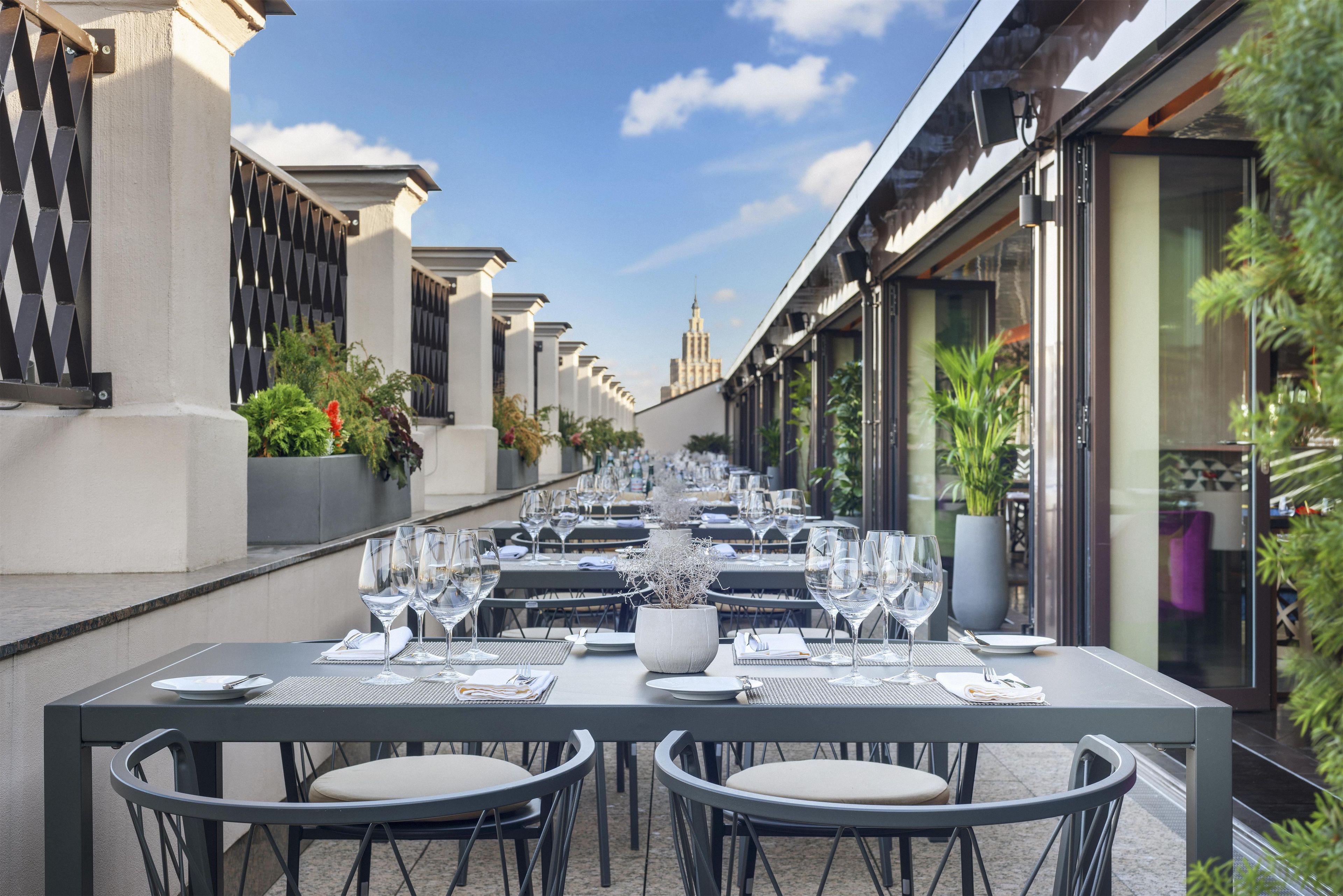 Un espace de restauration en plein air avec des tables prévues pour deux personnes, présentant un design moderne avec des chaises en métal et un vase central.