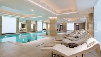 A modern indoor swimming pool with lounge chairs and a spa area.