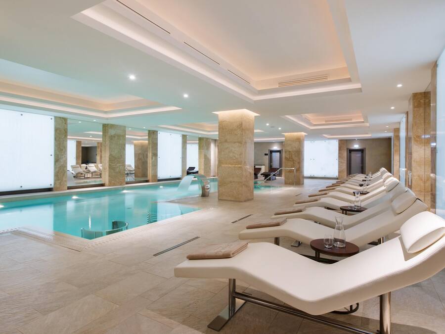 A modern indoor swimming pool with lounge chairs and a spa area.