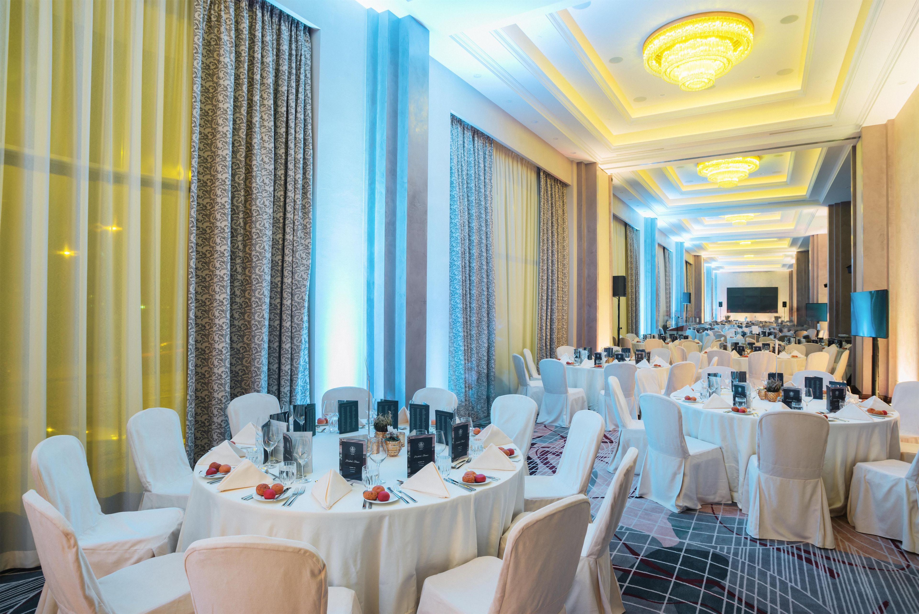 Un salón de banquetes con mesas redondas, sillas blancas y candelabros.