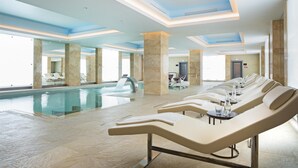 Vestíbulo de hotel con una amplia piscina interior, tumbonas y una zona de recepción.