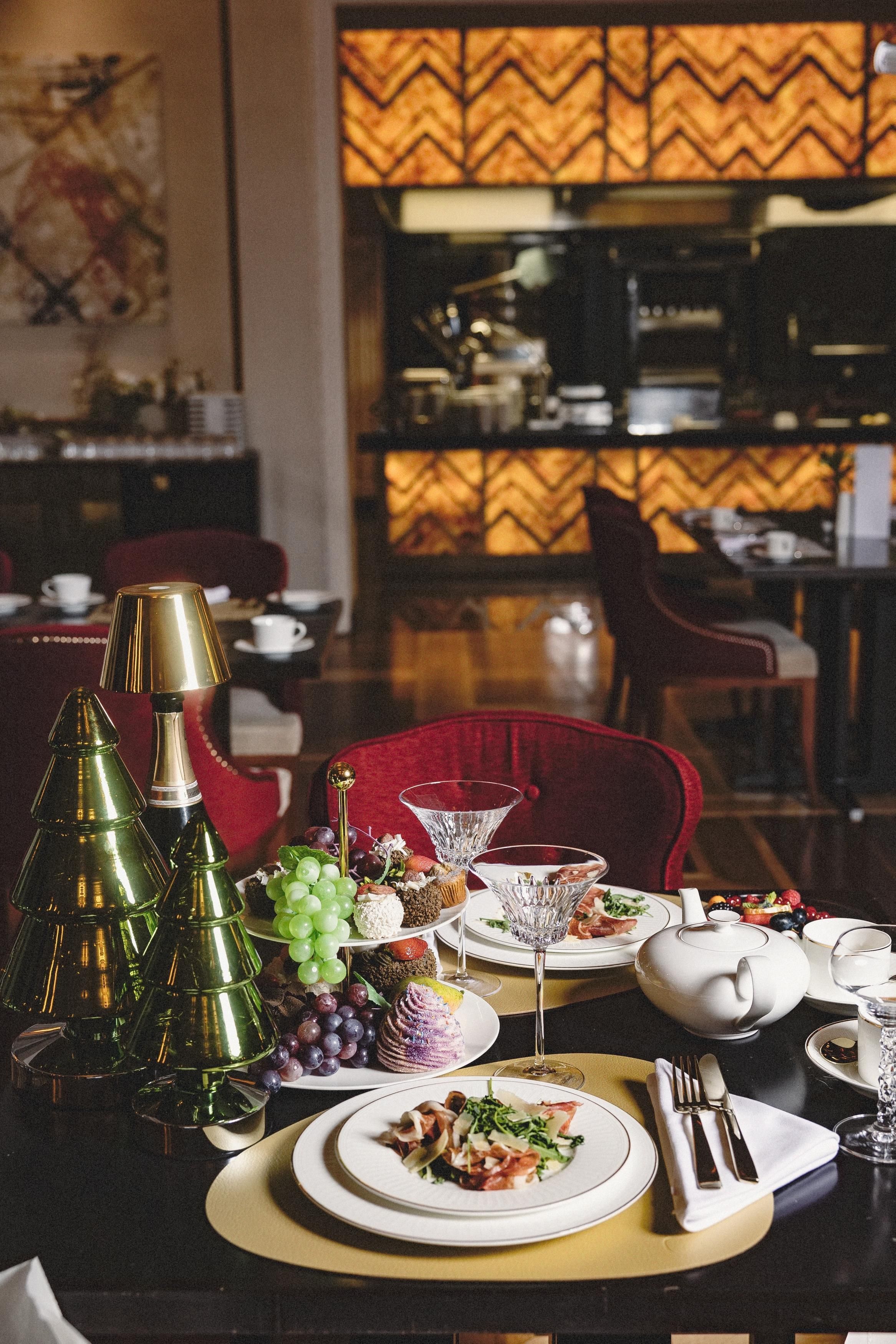 A dining table set with plates, cutlery, and a variety of food items, including grapes and a cake, in a restaurant setting.