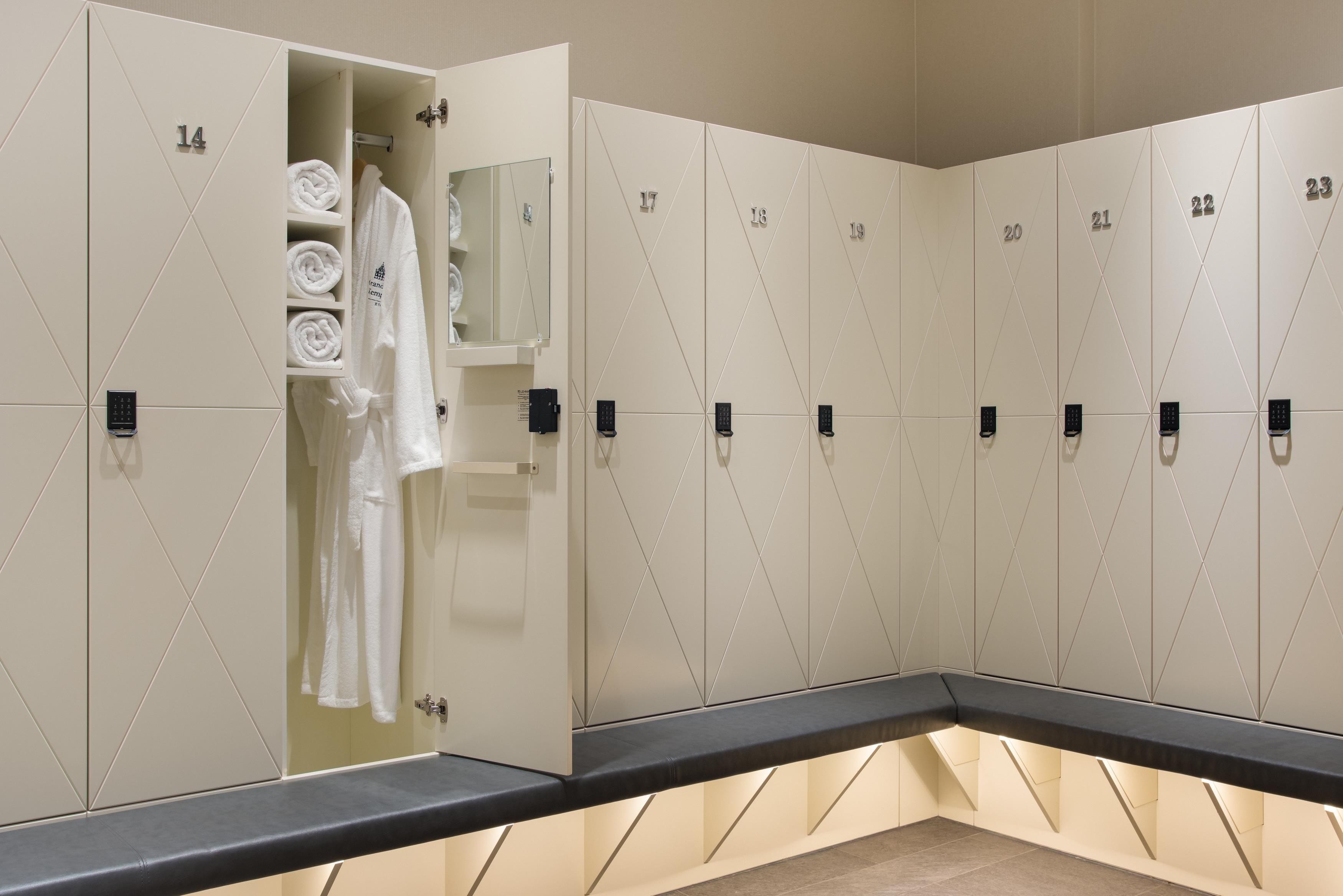 A row of lockers with numbers, a towel rack with folded towels, and a bench.