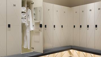 A row of lockers with numbers, a towel rack with folded towels, and a bench.