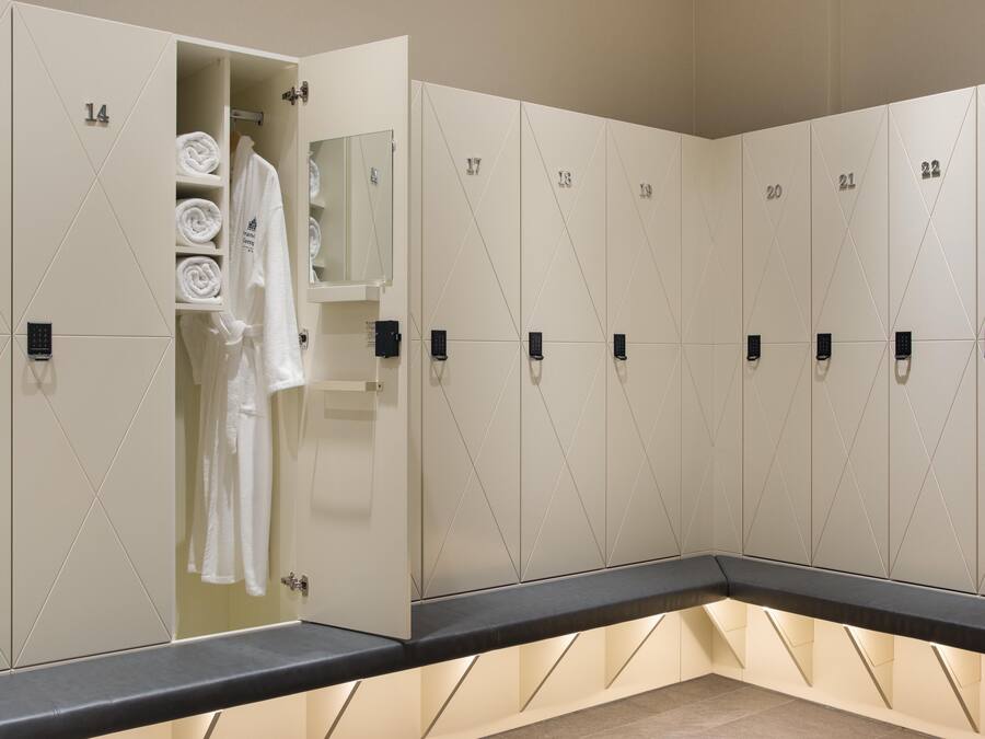 A row of lockers with numbers, a towel rack with folded towels, and a bench.