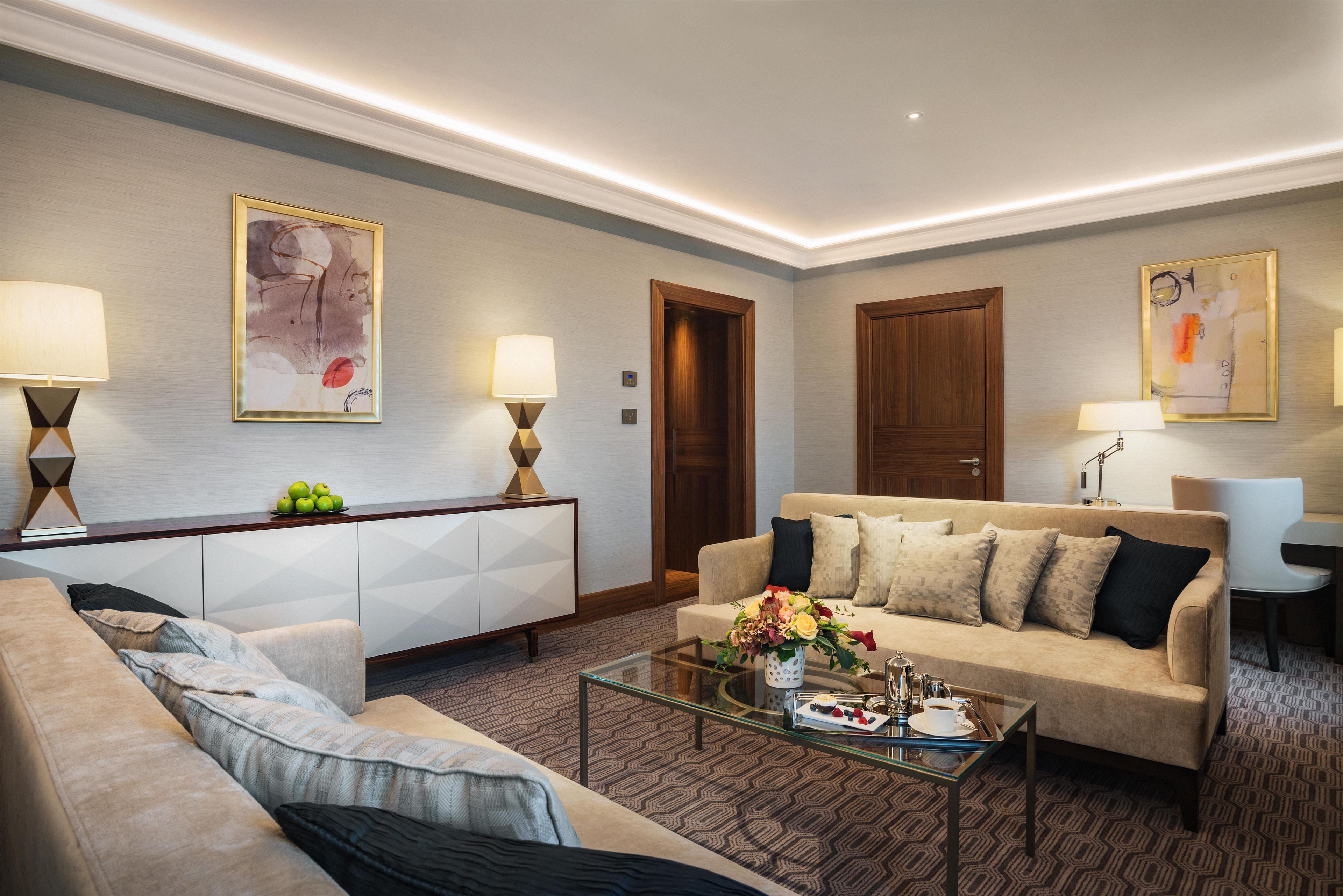 A modern living room with a sofa, a glass coffee table, and a cabinet. There are two wall-mounted lamps and a door.