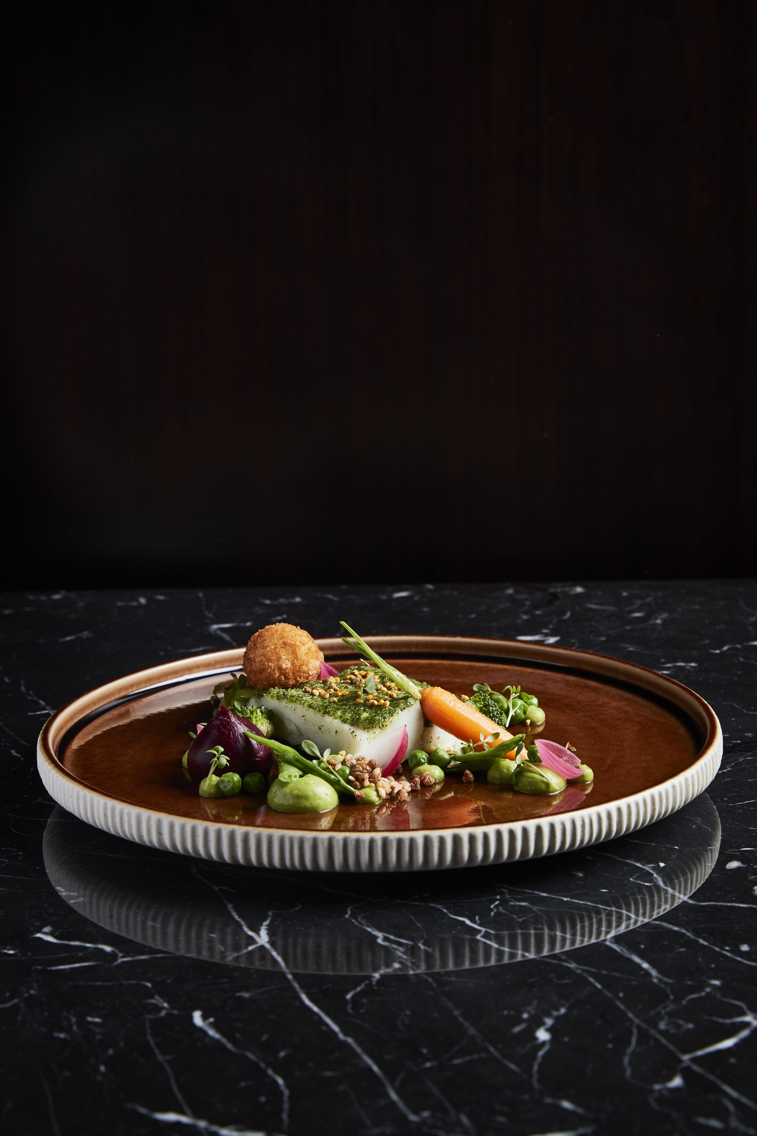 Une assiette contenant divers légumes et un objet sphérique, le tout posé sur une surface en marbre foncé.