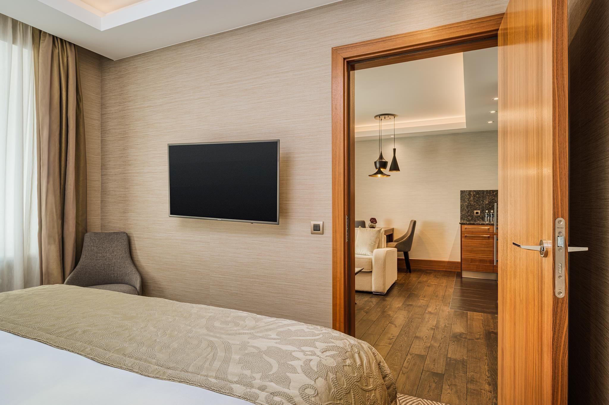 Habitació d'hotel amb un llit, un televisor fixat a la paret, una porta de fusta i vista a la zona de dinar.