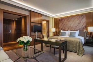 A hotel room with a bed, a desk with a laptop, a TV, and a vase with flowers. - Grand Hotel Kempinski Riga (Riga)