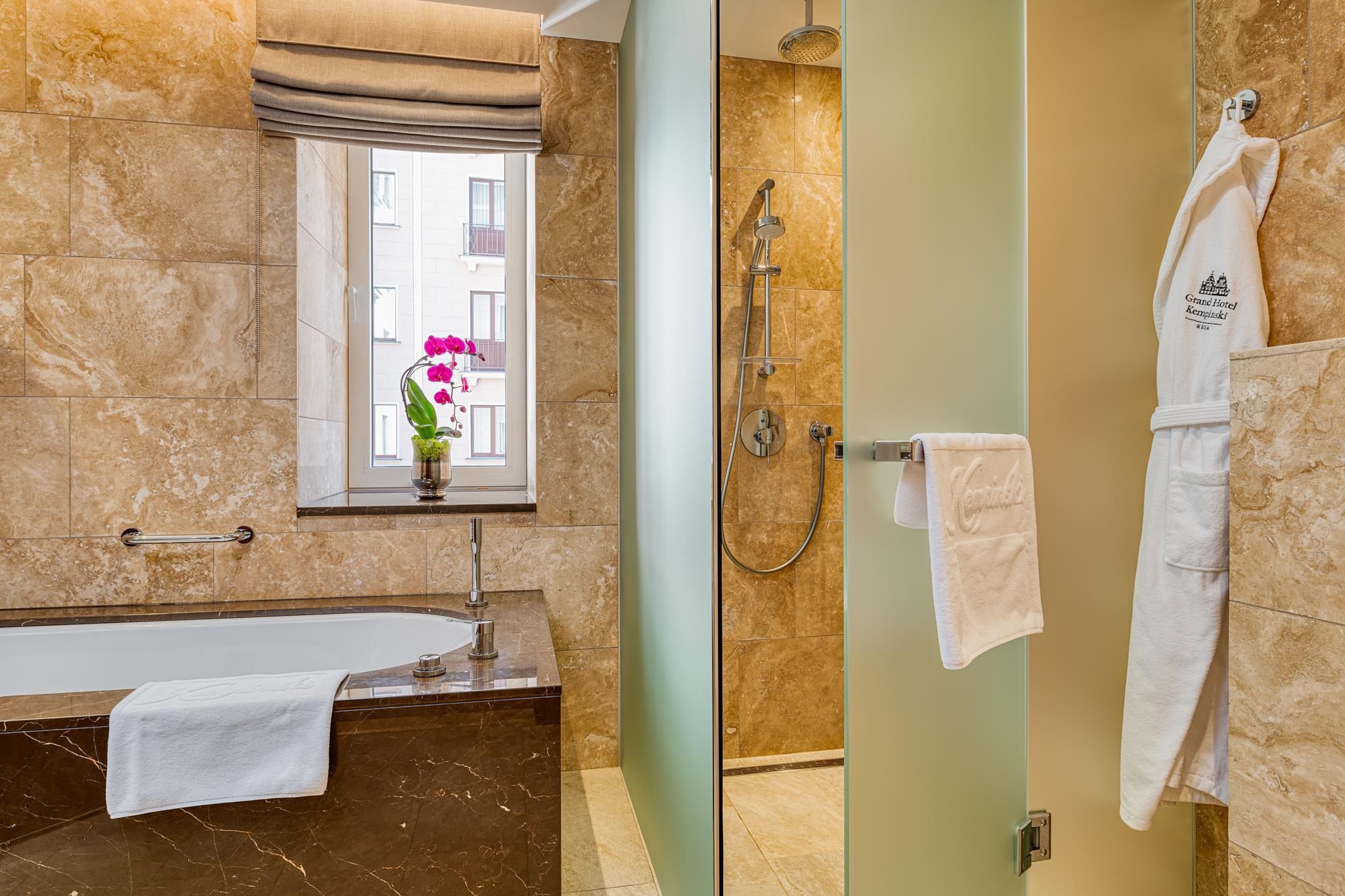 A modern bathroom with a bathtub, a glass-enclosed shower, and a window with a view of buildings.