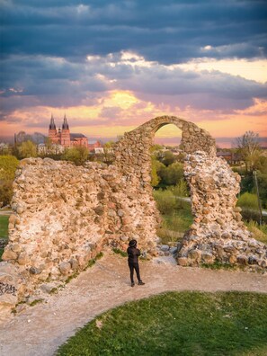 A historical stone archway in a park with a church in the background.