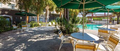 Un patio al aire libre con mesas, sillas, sombrillas y una piscina.