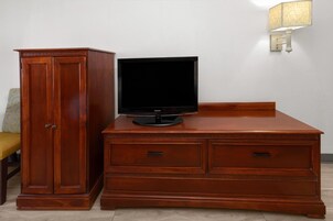 Un mueble de madera con un televisor de pantalla plana encima, una lámpara en la pared y una silla con un cojín estampado.