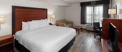 Camera d'albergo con un letto grande, una scrivania, una sedia, una TV e una finestra con tende.
