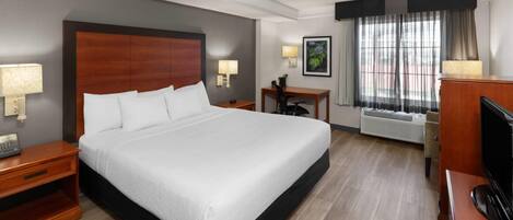 Habitación de hotel con una cama grande, mesitas de noche, un escritorio, una silla, un televisor y una ventana con cortinas.