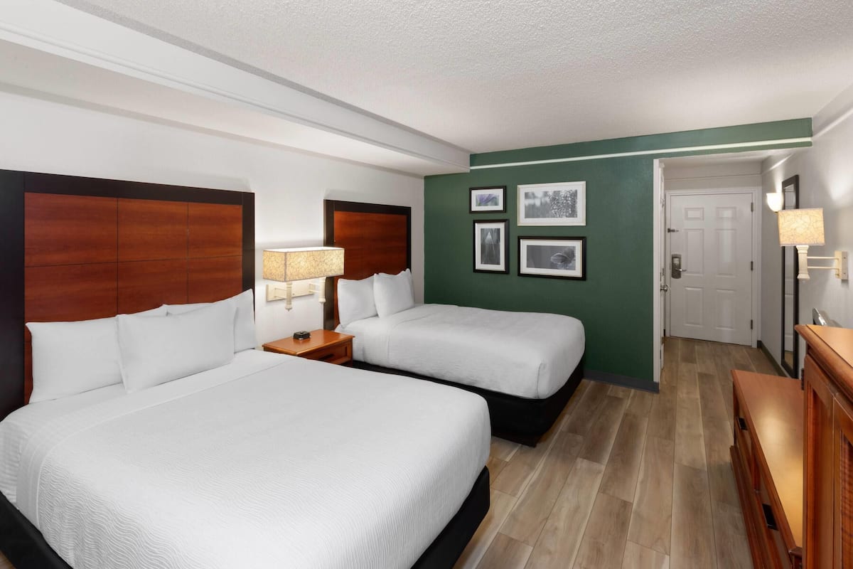 Ein Hotelzimmer mit zwei Betten, einem hölzernen Kopfteil, einer grünen Akzentwand und gerahmten Bildern.