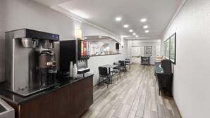 A modern hotel lobby with a coffee station, seating area, and a reception desk.