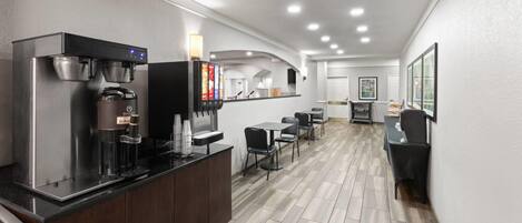 A modern hotel lobby with a coffee station, seating area, and a reception desk.